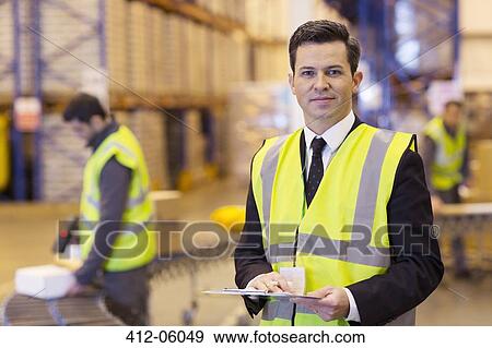 Stock Photo - Businessman holding clipboard in warehouse. Fotosearch