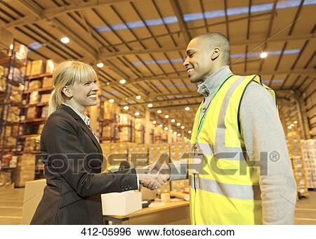 Businesswoman and worker shaking hands in warehouse View Large Photo Image Stock Photograph - Businesswoman and worker shaking hands in warehouse. Fotosearch