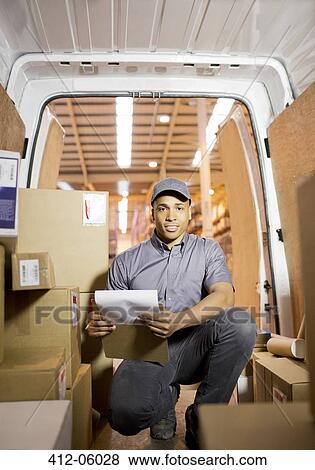 Stock Photo - Delivery boy checking boxes in van. Fotosearch