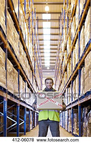 Stock Photo - Worker carrying "urgent" box in warehouse. Fotosearch