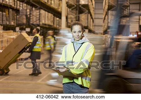 Stock Image - Worker holding clipboard in warehouse. Fotosearch