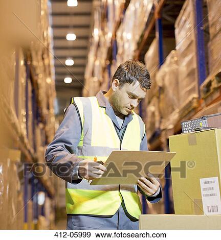 Stock Photo - Worker reading clipboard in warehouse. Fotosearch