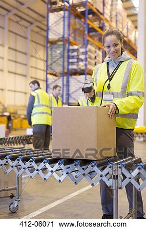 Stock Image - Worker scanning box on conveyor belt in warehouse. Fotosearch