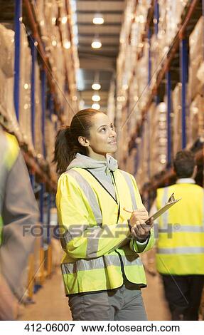 Stock Photo - Worker writing on clipboard in warehouse. Fotosearch