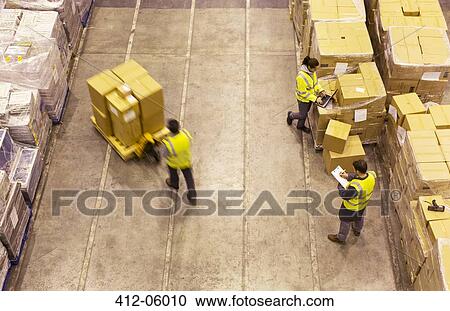 Workers carting boxes in warehouse View Large Photo Image Stock Image - Workers carting boxes in warehouse. Fotosearch