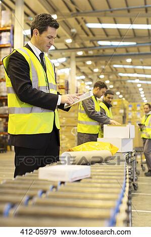 Stock Photo - Workers checking packages on conveyor belt in warehouse. Fotosearch