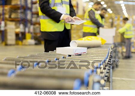 Stock Photo - Workers checking packages on conveyor belt in warehouse. Fotosearch