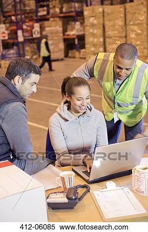 Stock Photography - Workers using laptop in warehouse. Fotosearch