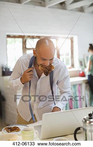 Businessman eating breakfast and using laptop View Large Photo Image Stock Image - Businessman eating breakfast and using laptop. Fotosearch