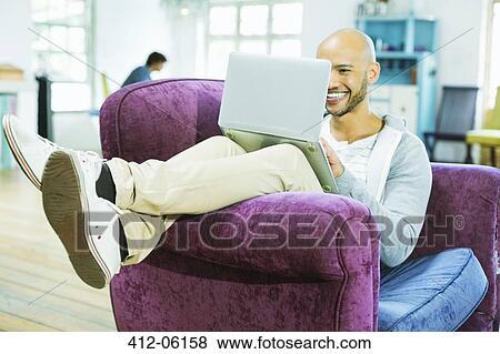 Man using laptop in armchair View Large Photo Image Stock Photo - Man using laptop in armchair. Fotosearch