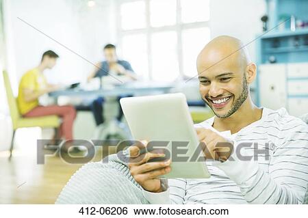 Man using tablet computer in living room View Large Photo Image Stock Photograph - Man using tablet computer in living room. Fotosearch