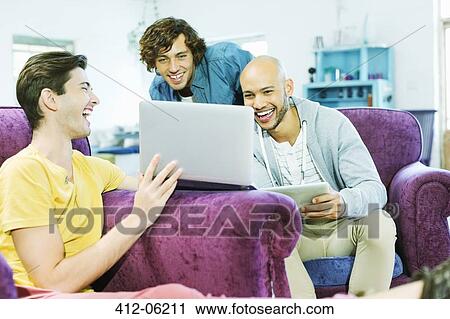 Stock Image - Men using laptop together in living room. Fotosearch