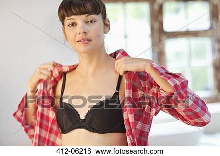 Stock Photograph - Woman putting on shirt in bedroom. Fotosearch