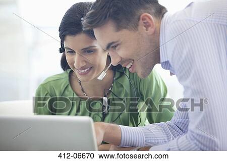 Stock Image - Business people using laptop together in office. Fotosearch