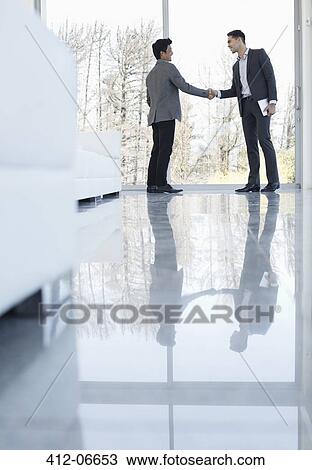 Stock Image - Businessmen shaking hands in office. Fotosearch