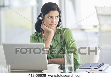 Stock Photo - Businesswoman wearing headphones at desk. Fotosearch