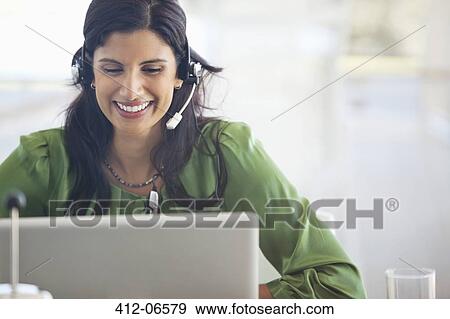 Stock Photo - Businesswoman wearing headset at desk. Fotosearch