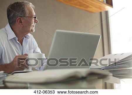 Stock Image - Businessman having cup of coffee at laptop. Fotosearch