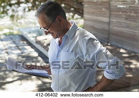 Stock Image - Businessman reading papers outdoors. Fotosearch