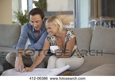 Stock Photograph - Couple examining blueprints on sofa. Fotosearch
