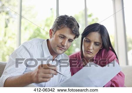 Stock Image - Couple reading papers together on sofa. Fotosearch