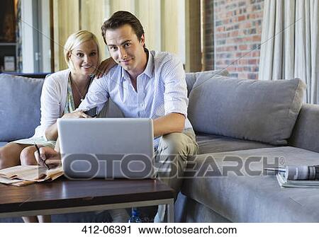 Stock Image - Couple using laptop together on sofa. Fotosearch