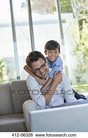 Stock Photograph - Father and son using laptop on sofa. Fotosearch