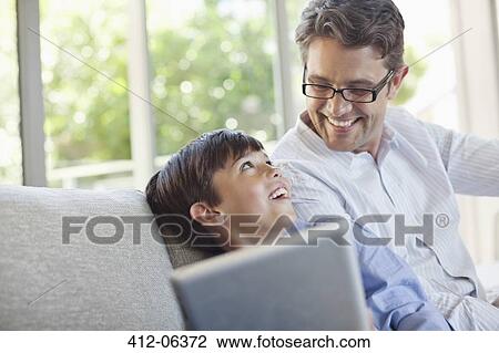 Stock Image - Father and son using tablet computer on sofa. Fotosearch