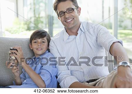 Stock Image - Father and son with change jar on sofa. Fotosearch