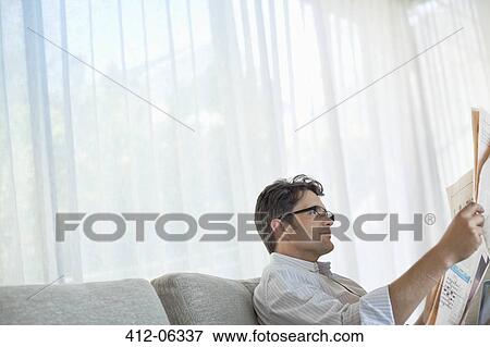 Stock Photo - Man reading newspaper on sofa. Fotosearch