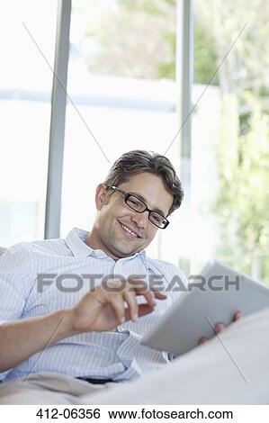 Man using tablet computer on sofa View Large Photo Image Stock Photograph - Man using tablet computer on sofa. Fotosearch