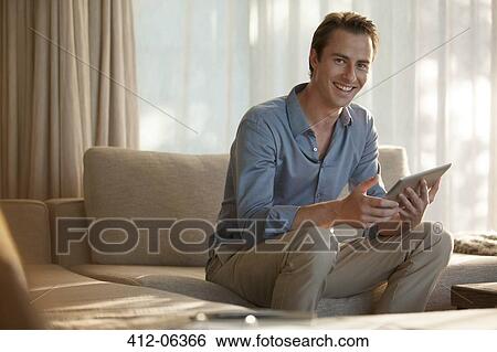 Stock Photograph - Man using tablet computer on sofa. Fotosearch
