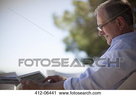 Stock Image - Older man using tablet computer outdoors. Fotosearch