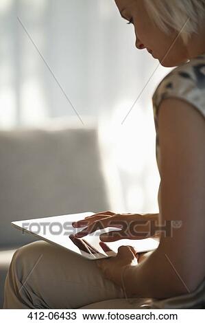 Stock Image - Woman using tablet computer on sofa. Fotosearch