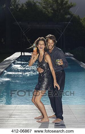 Stock Photo - Couple having drinks by swimming pool. Fotosearch