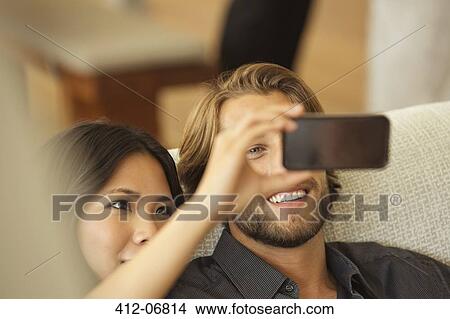 Picture - Couple using cell phone as camera together on sofa. Fotosearch