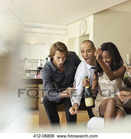 Stock Photograph - Friends opening bottle of champagne together. Fotosearch