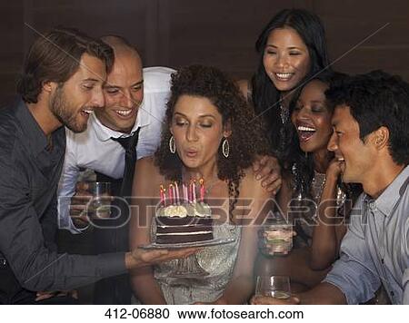Stock Image - Woman blowing out birthday candles at party. Fotosearch