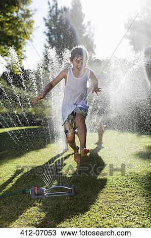 Boy playing in sprinkler in backyard View Large Photo Image Stock Image - Boy playing in sprinkler in backyard. Fotosearch