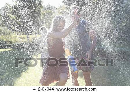 Picture - Couple playing in sprinkler in backyard. Fotosearch