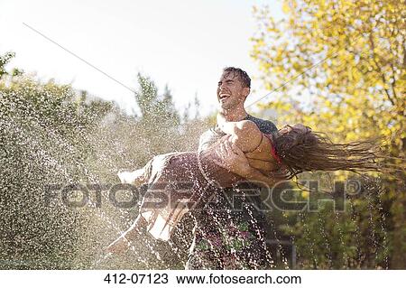Couple playing in sprinkler in backyard View Large Photo Image Stock Image - Couple playing in sprinkler in backyard. Fotosearch