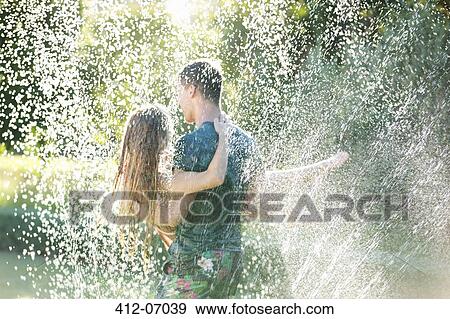 Couple playing in sprinkler in backyard View Large Photo Image Stock Photo - Couple playing in sprinkler in backyard. Fotosearch