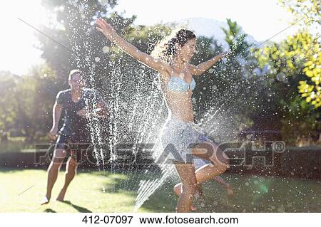 Couple playing in sprinkler in backyard View Large Photo Image Stock Photo - Couple playing in sprinkler in backyard. Fotosearch