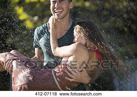 Couple playing in sprinkler in backyard View Large Photo Image Stock Photo - Couple playing in sprinkler in backyard. Fotosearch