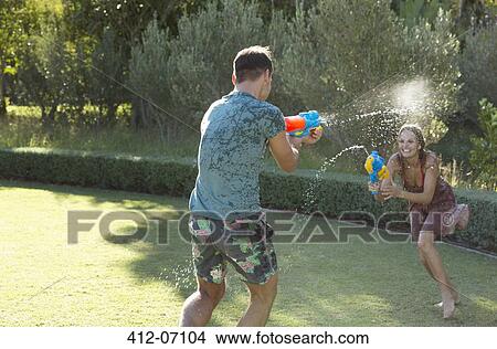 Couple playing with water guns in backyard View Large Photo Image Picture - Couple playing with water guns in backyard. Fotosearch