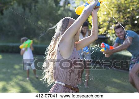 Stock Image - Family playing with water guns in backyard. Fotosearch