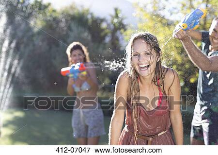 Stock Photo - Friends playing with water guns in backyard. Fotosearch