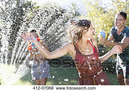 Friends playing with water guns in sprinkler View Large Photo Image Stock Photo - Friends playing with water guns in sprinkler. Fotosearch