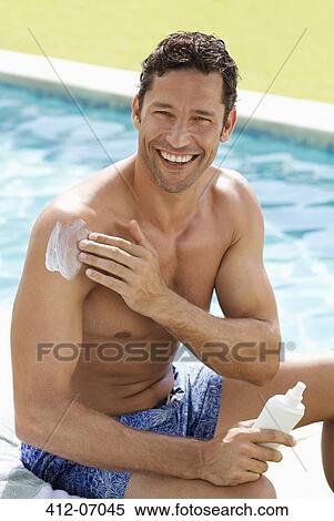 Stock Photography - Man applying sunscreen by swimming pool. Fotosearch