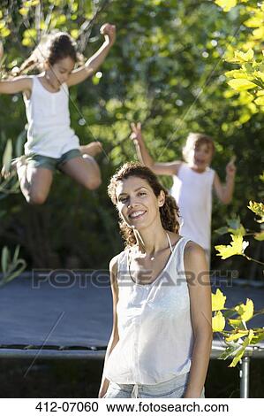 Stock Image - Mother standing by children on trampoline. Fotosearch